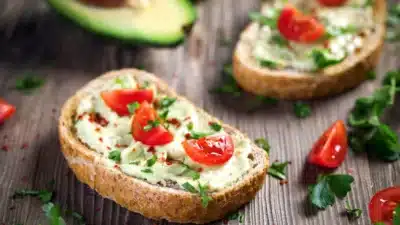 Avocado toast with cherry tomatoes and herbs on rustic bread, garnished with spices, on a wooden table.