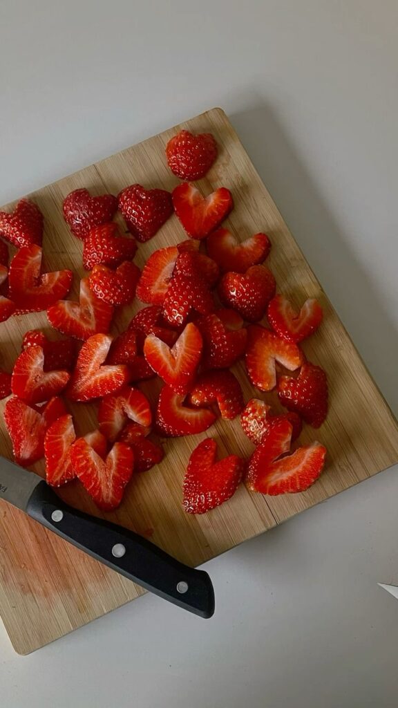 Heart-shaped strawberries on a wooden board with a knife, creating a lovely food presentation.