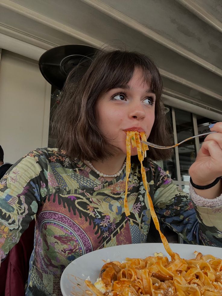 Woman enjoying pasta at a restaurant, wearing a colorful patterned shirt.