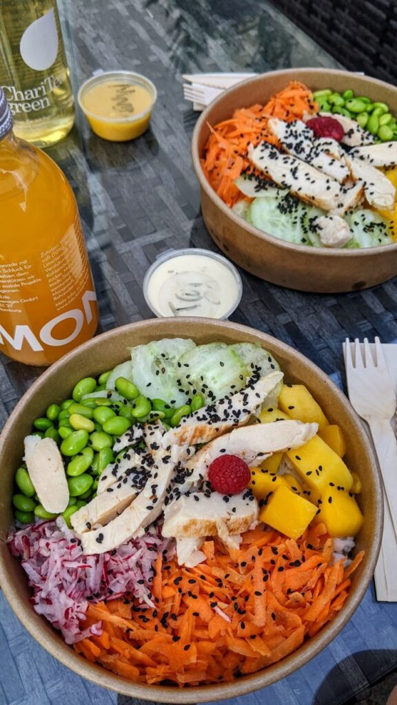 Colorful healthy poke bowls with chicken, edamame, mango, and carrots served with drinks on a table.