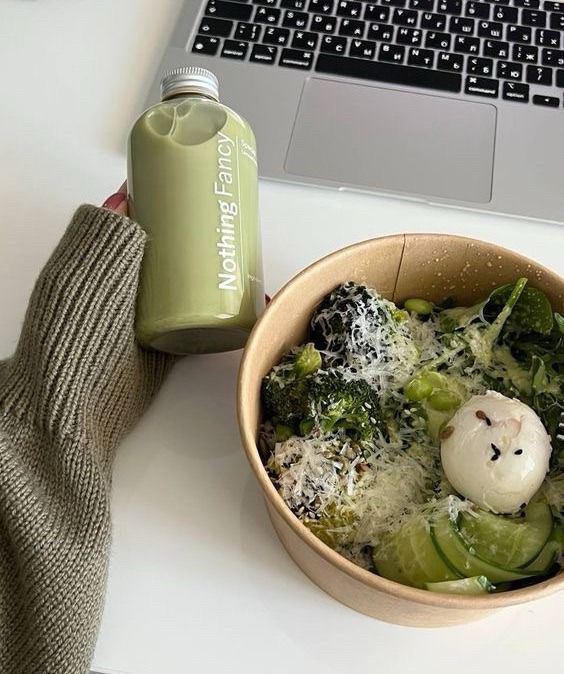 Healthy salad with greens and poached egg beside a green smoothie bottle, positioned in front of a laptop.