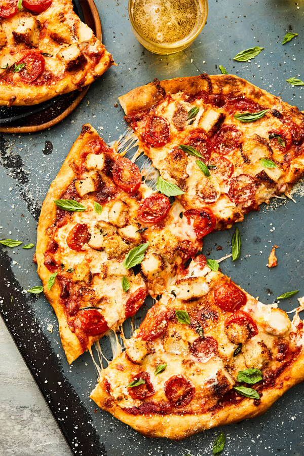 Delicious pepperoni pizza with fresh basil and cheese, served with a glass of beer on a rustic black board.
