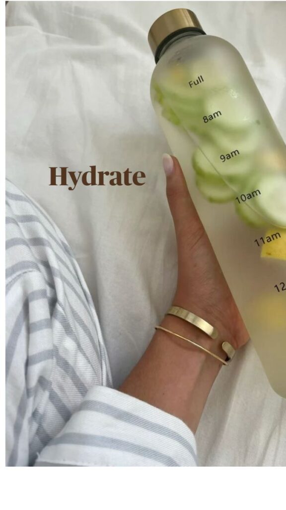 Hand holding a clear bottle with fruit and time markers on a bed with Hydrate text.