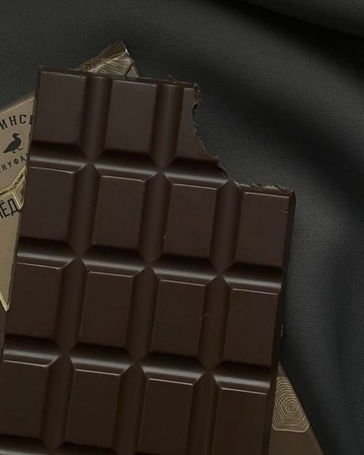 A partially eaten dark chocolate bar on gray fabric background, showcasing rich texture and indulgent flavor.