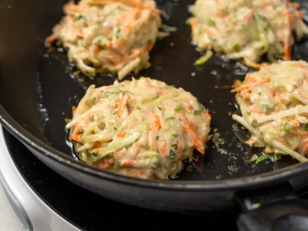 Vegetable fritters sizzling in a skillet, filled with shredded carrots and zucchini, for a delicious vegetarian dish.