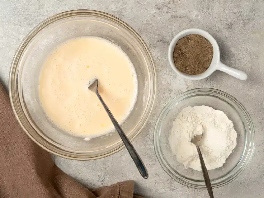 Batter preparation with flour, eggs, and seasoning in bowls on a kitchen countertop for cooking or baking.
