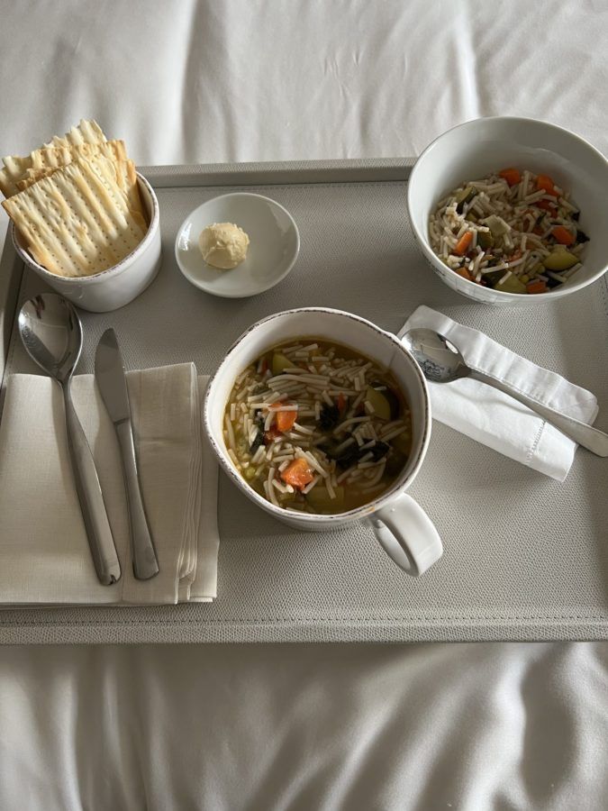 Bowl of noodle soup with vegetables, served with crispbread and butter on a tray with cutlery.