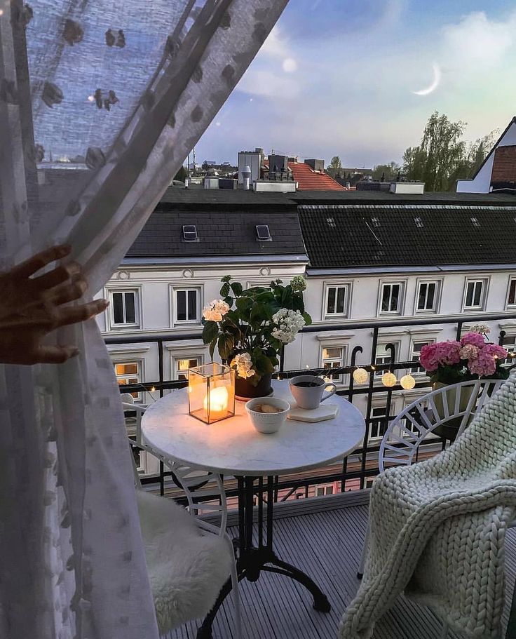 Cozy balcony with candlelight and plants, overlooking cityscape at twilight. Perfect for relaxation and evening coffee.