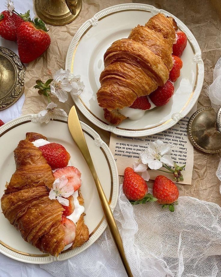 Croissants with strawberries and cream on elegant plates, garnished with flowers. Perfect for a delightful brunch setting.