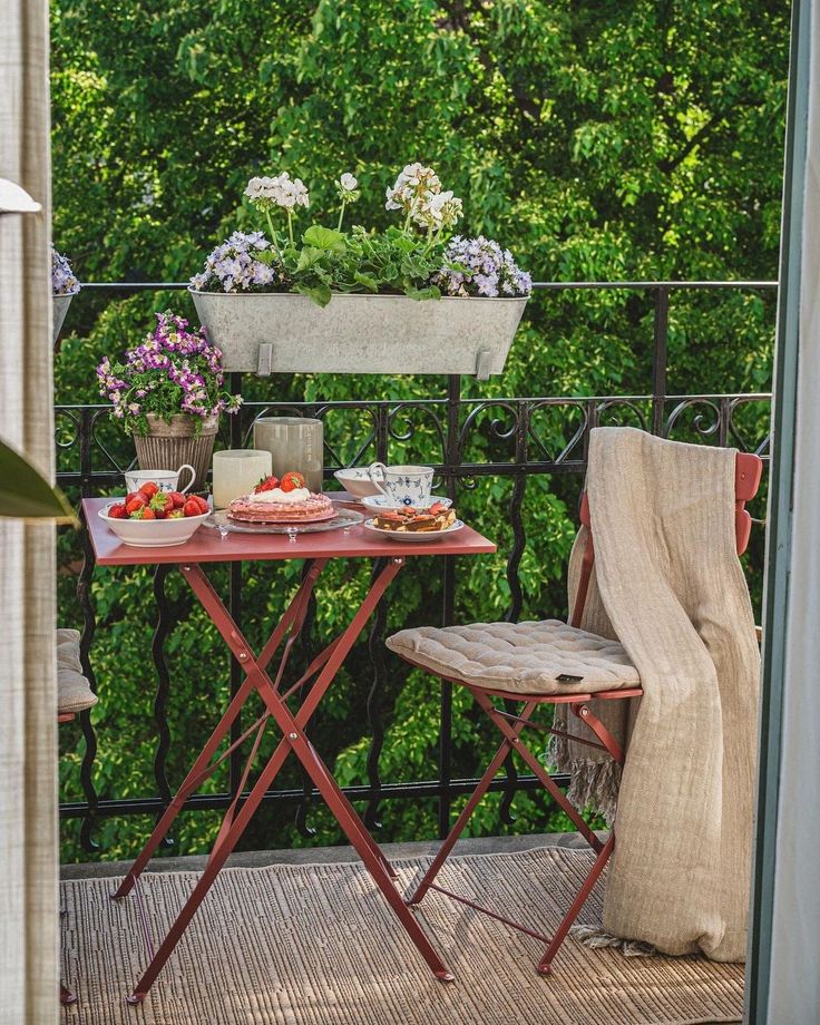 Cozy balcony breakfast setup with flowers, table, and chairs overlooking lush greenery. Ideal for relaxation.