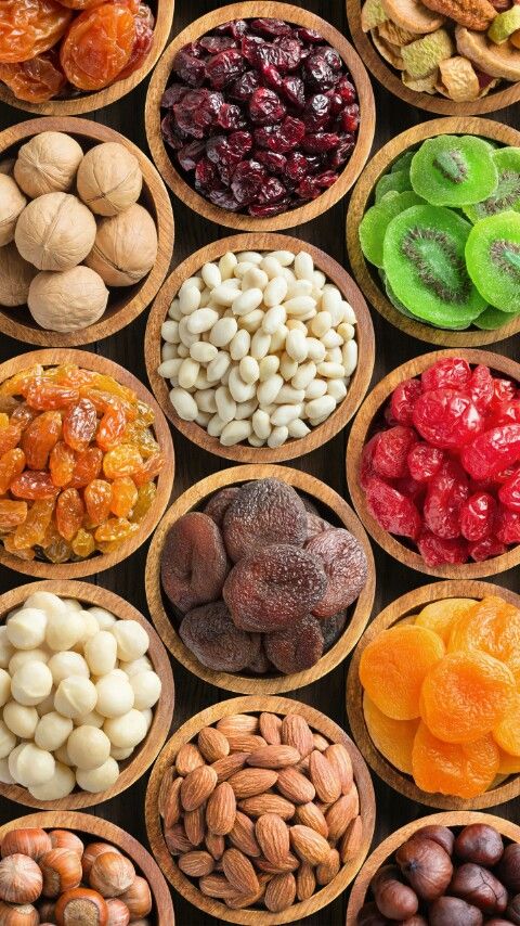 Assorted dried fruits and nuts in wooden bowls, featuring apricots, almonds, and kiwi slices. Perfect for healthy snacking.