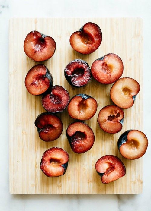 Halved ripe plums arranged on a wooden board, showcasing vibrant red and purple hues. Perfect for recipes or healthy snacks.