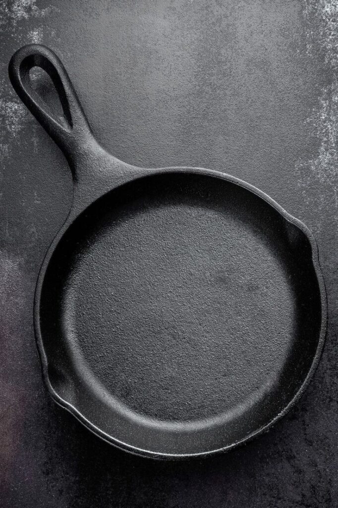 Cast iron skillet on dark background, top view. Perfect for cooking or frying. Durable and versatile kitchen tool.