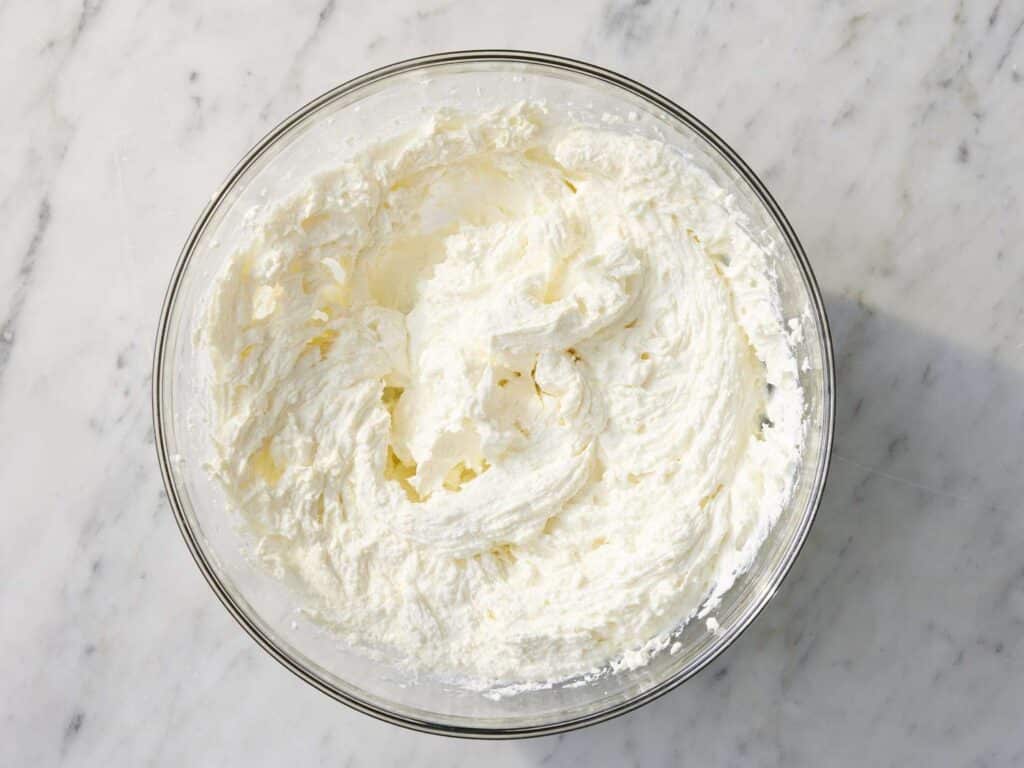 Fluffy whipped cream in a glass bowl on a marble countertop, perfect for desserts and baking recipes.