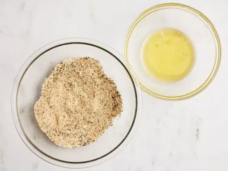 Bowl of almond flour beside bowl of egg whites on a marble surface, ready for baking gluten-free treats.