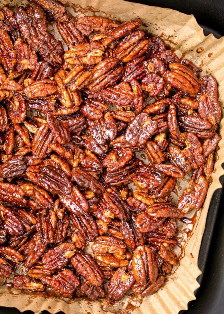 Close-up of roasted candied pecans on parchment paper, glistening with a sweet glaze, perfect for snacks or desserts.