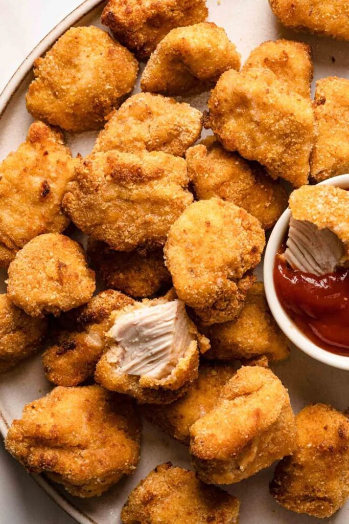 Golden crispy chicken nuggets with dipping sauce on a plate.