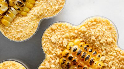 Close-up of grilled corn with creamy topping in a cup, topped with crumbled cheese, showcasing a delicious street food treat.