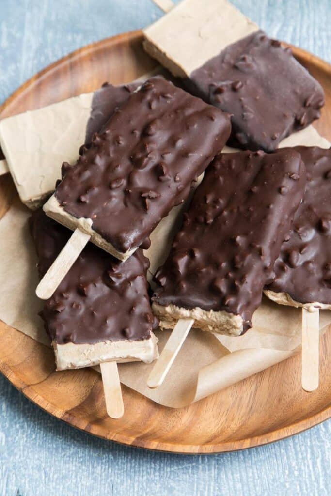 Chocolate-covered ice cream bars on a wooden plate, tempting dessert for a hot day.