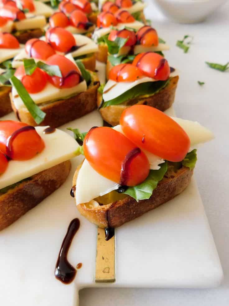 Slices of bruschetta topped with cherry tomatoes, cheese, and balsamic glaze on a marble board.