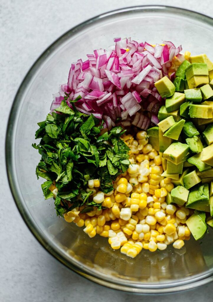 Bowl with chopped red onion, avocado, cilantro, and corn. Fresh ingredients for a colorful salad or salsa.