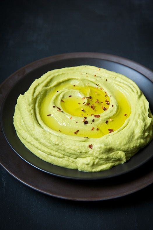 Creamy avocado hummus garnished with olive oil and chili flakes in a dark bowl, perfect for a healthy snack.