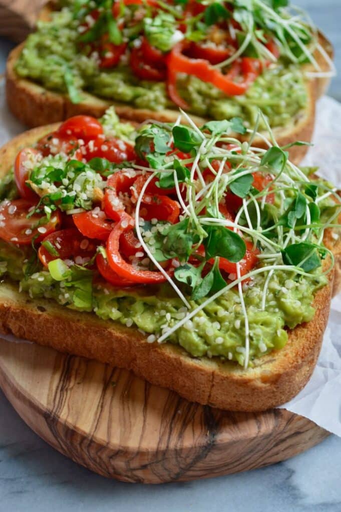 Avocado toast topped with cherry tomatoes and microgreens on a wooden board, perfect for a healthy breakfast.