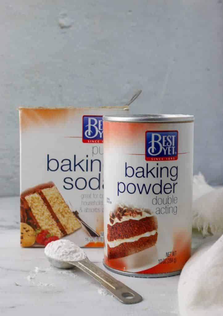 Baking soda and baking powder with a measuring spoon on a marble countertop, ideal for baking recipes.