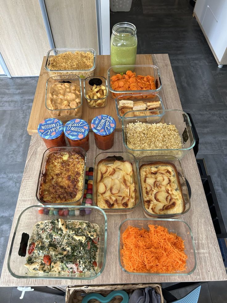 Assorted homemade dishes on a wooden table, featuring gratins, casseroles, salads, and jars for a meal prep session.