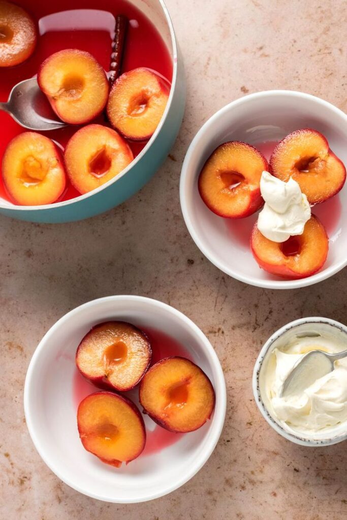 Halved poached plums in syrup with dollop of cream, served in bowls for a delicious dessert treat.