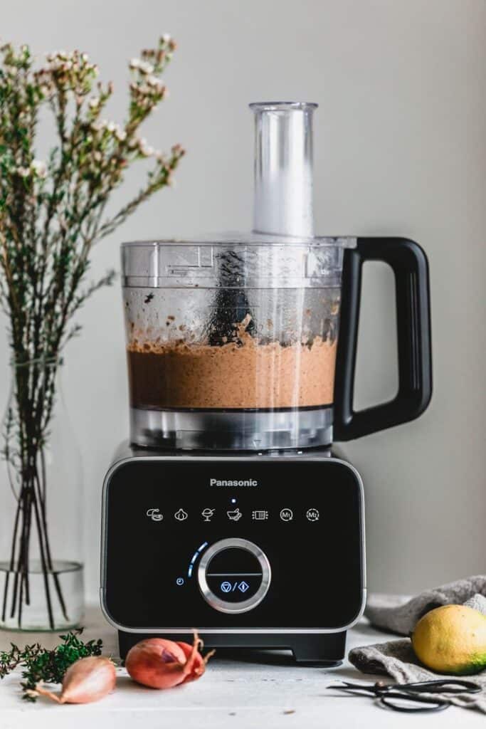 Modern food processor blending ingredients on a kitchen counter with fresh herbs and vegetables nearby.