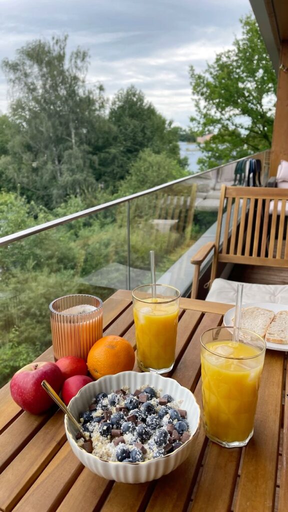 Healthy outdoor breakfast with oatmeal, fruits, and orange juice on a wooden table overlooking a lush green view.