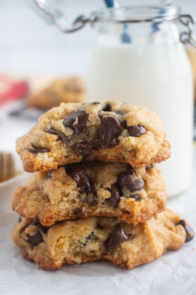 Stack of chocolate chip cookies with a glass of milk in the background, perfect for a sweet treat.