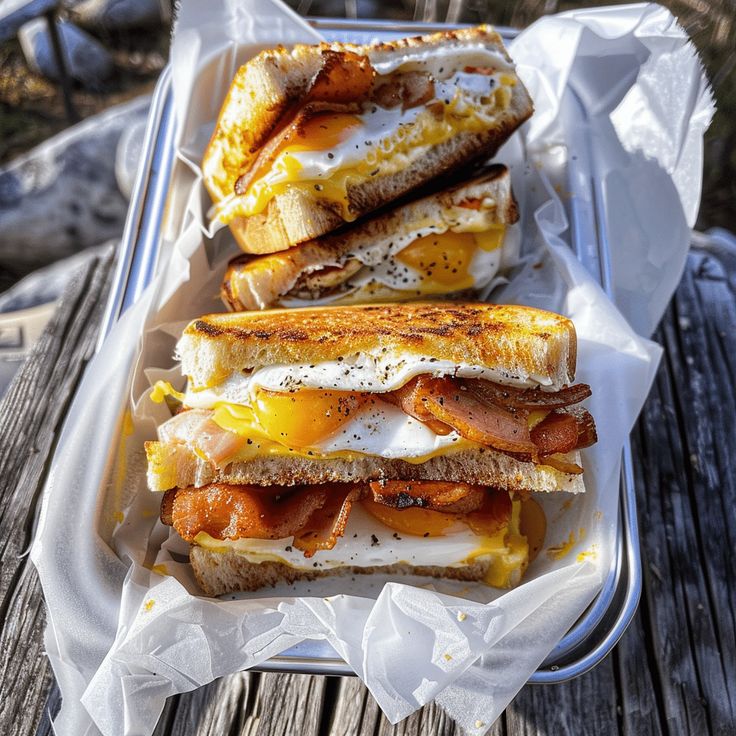 Breakfast sandwich with crispy bacon, sunny-side eggs, and melted cheese stacked in a tray for a delicious morning meal.