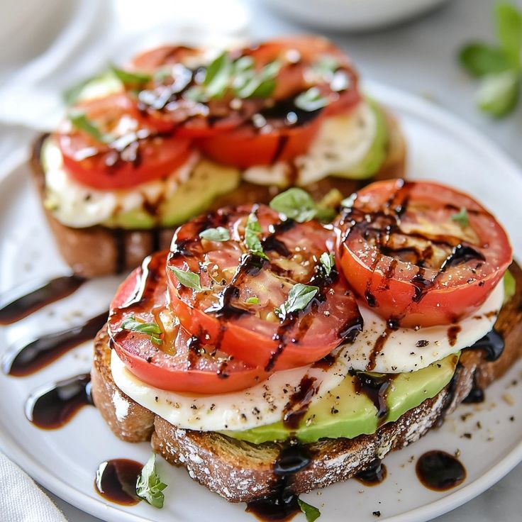 Avocado toast with sliced tomatoes, mozzarella, and balsamic glaze on a white plate, garnished with fresh herbs.