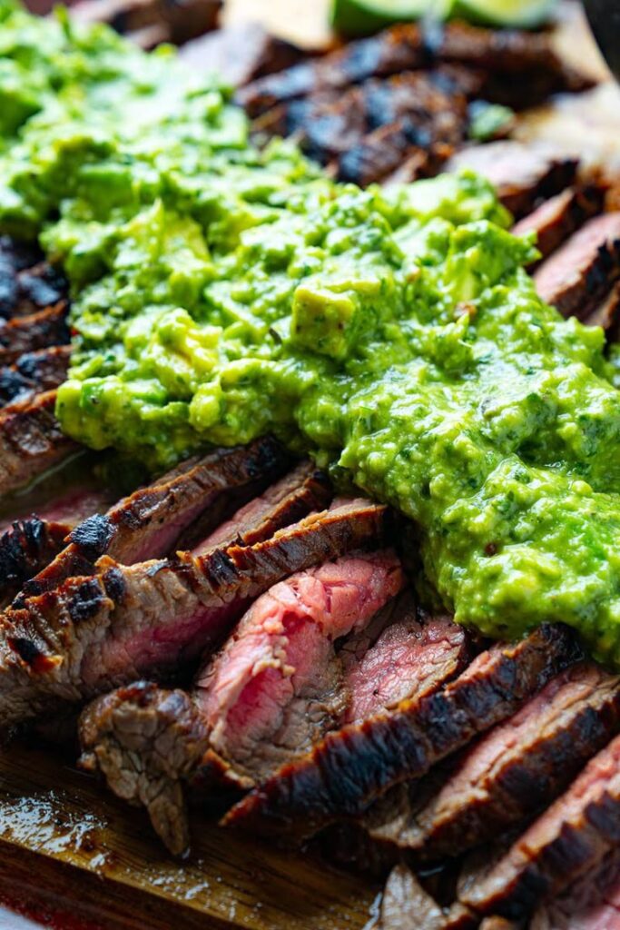 Grilled steak topped with fresh avocado salsa, vibrant and appetizing, served on a wooden board.