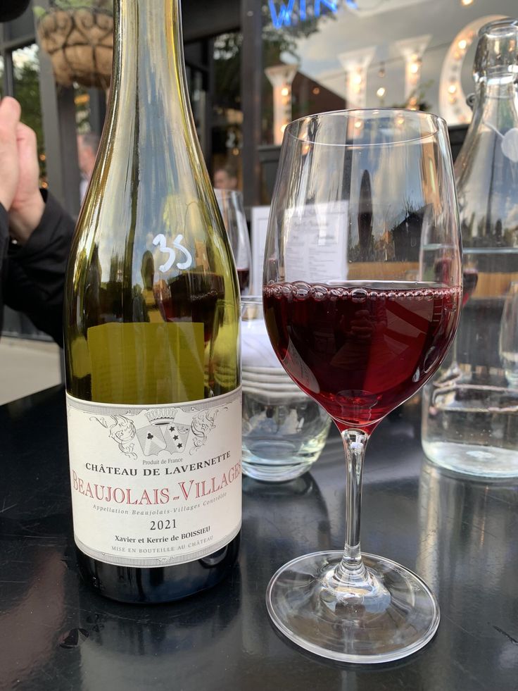 Bottle and glass of Château de Lavernette Beaujolais-Villages 2021 wine on an outdoor table.