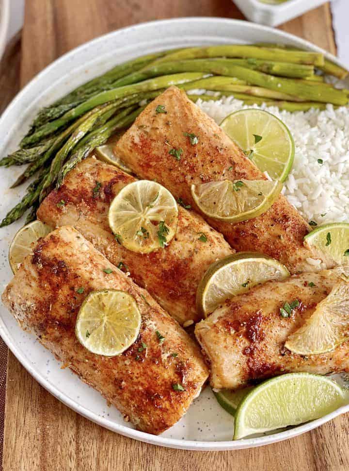 Grilled salmon with lime, asparagus, and rice on a white plate for a healthy, delicious meal option.
