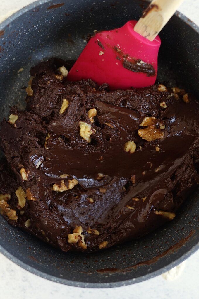 Chocolate brownie batter with walnuts in a pan, mixed with a red spatula. Rich, gooey texture. Perfect for baking.