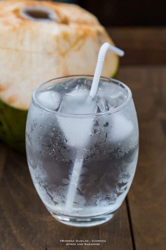 Fresh coconut water in a glass with ice and straw, refreshing drink on a wooden table background.