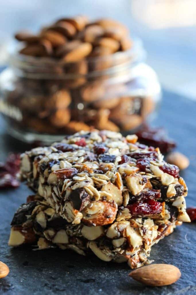 Nut and fruit granola bars stacked with almonds in a jar; a healthy and tasty snack option.