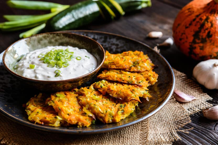 Crispy vegetable fritters served with creamy dip garnished with green onions on rustic wooden table.