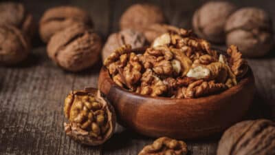 Rustic wooden bowl filled with shelled walnuts on a rustic wooden table, surrounded by whole walnuts.
