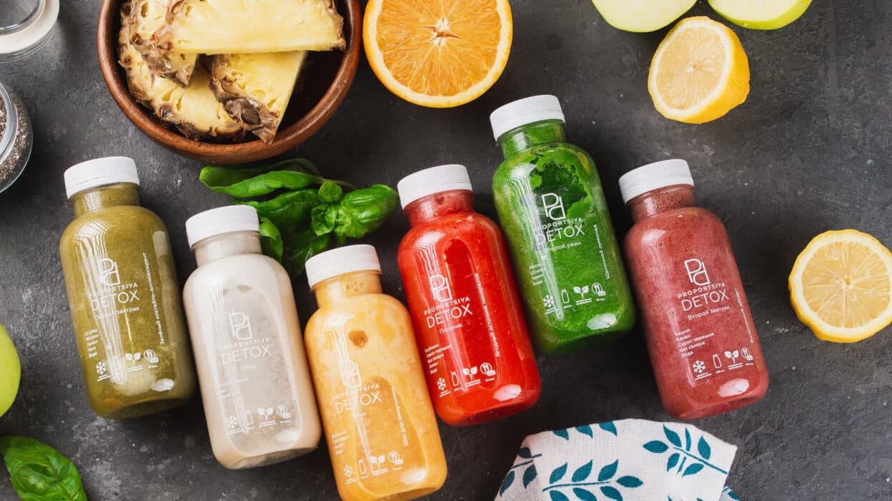 Colorful detox juice bottles with fresh fruit slices on a dark background, promoting healthy lifestyle choices.