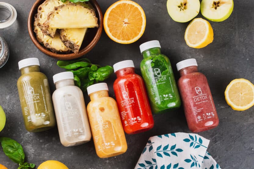 Colorful detox juice bottles with fresh fruit slices on a dark background, promoting healthy lifestyle choices.
