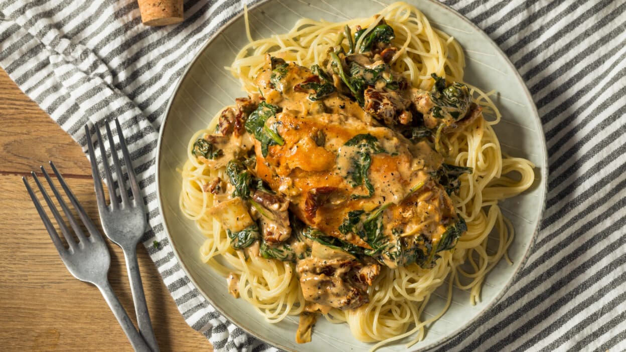 Creamy Tuscan chicken pasta with spinach and sun-dried tomatoes on a plate, served with a striped napkin.