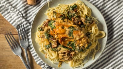 Creamy Tuscan chicken pasta with spinach and sun-dried tomatoes on a plate, served with a striped napkin.