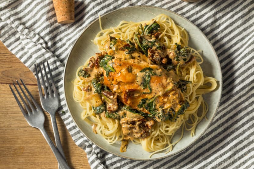 Creamy Tuscan chicken pasta with spinach and sun-dried tomatoes on a plate, served with a striped napkin.
