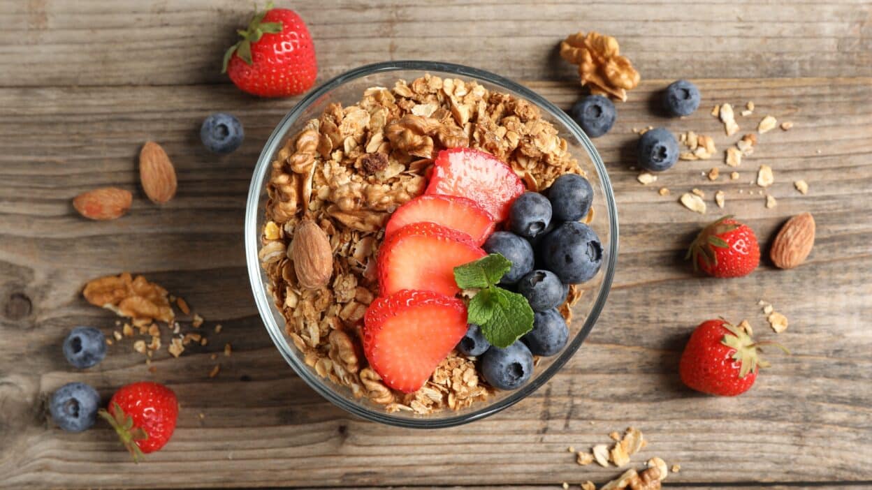 Bowl of granola with fresh strawberries, blueberries, and nuts on a wooden table. Healthy breakfast option.
