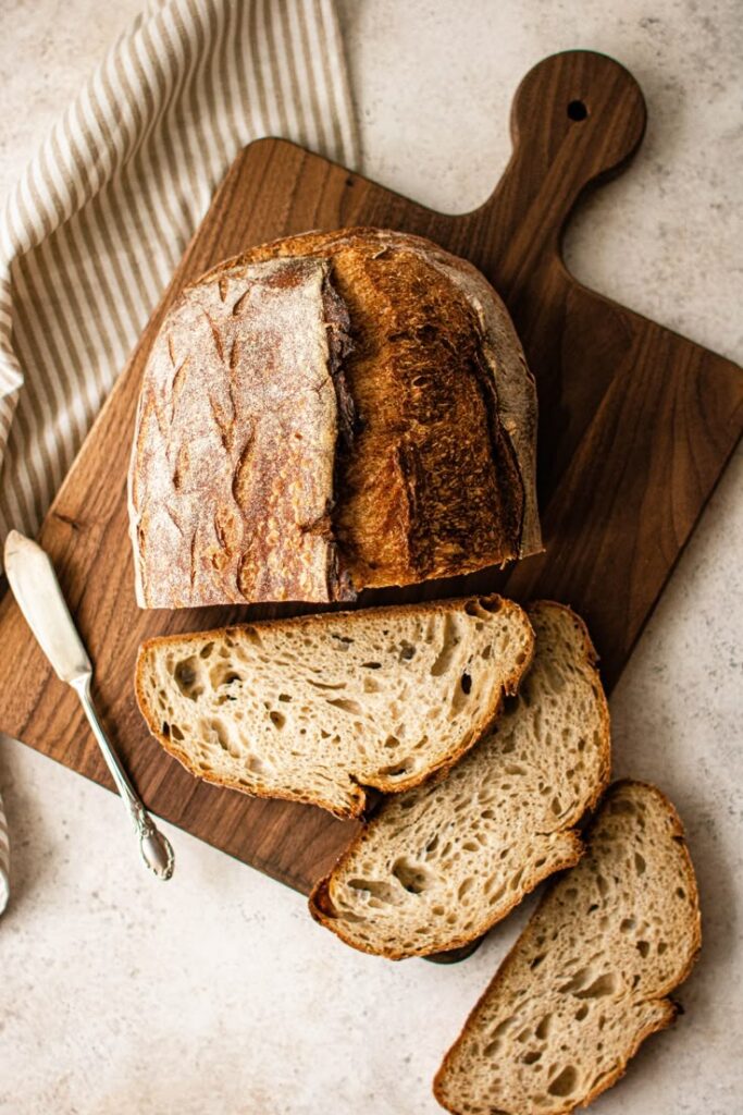 Rustic sourdough bread on a wooden board with sliced pieces and a knife, perfect for a cozy homemade meal.
